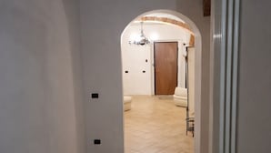 Un pasillo con suelo de baldosas, un radiador y una puerta que da a otra habitación.