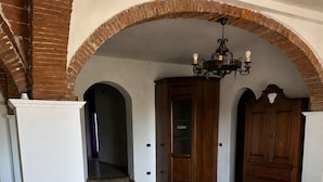 Una habitación amplia con suelo de baldosas, dos sillones blancos, un armario de madera y una araña.