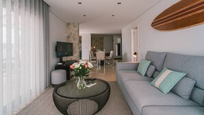 Een moderne woonkamer met een grijze bank, een ronde salontafel met een vaas, en een televisie op een dressoir.