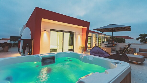 Een modern buitengebied met een hottub, een rood gebouw, een grote parasol en loungezitting.