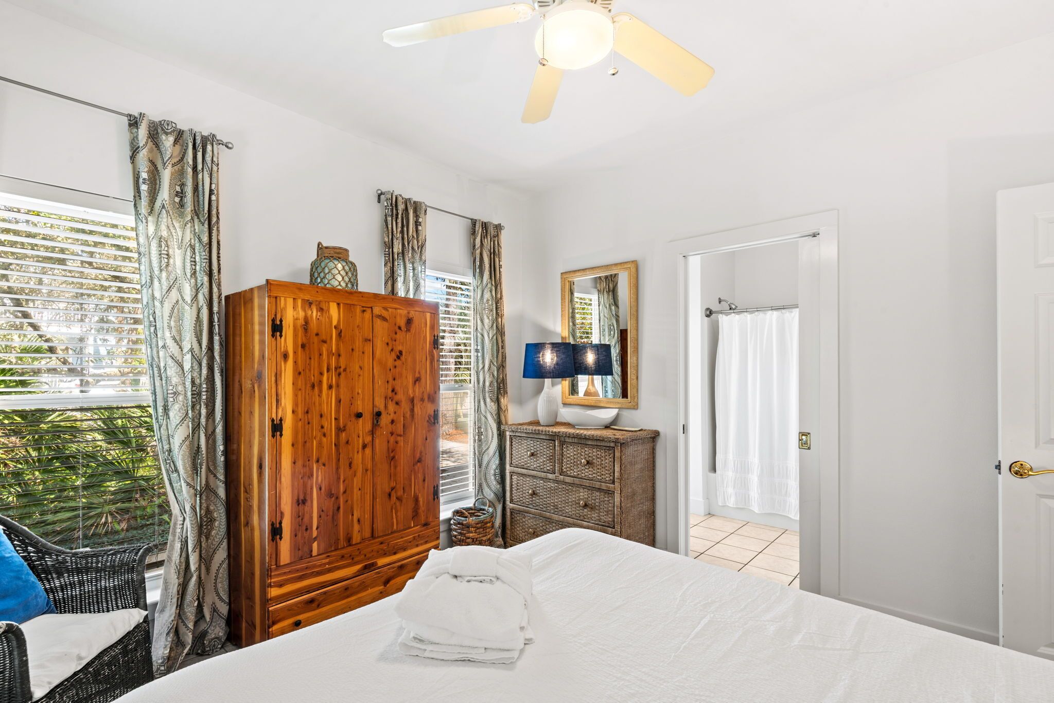 Quarto com cama, guarda-roupa de madeira, espelho e ventilador de teto.