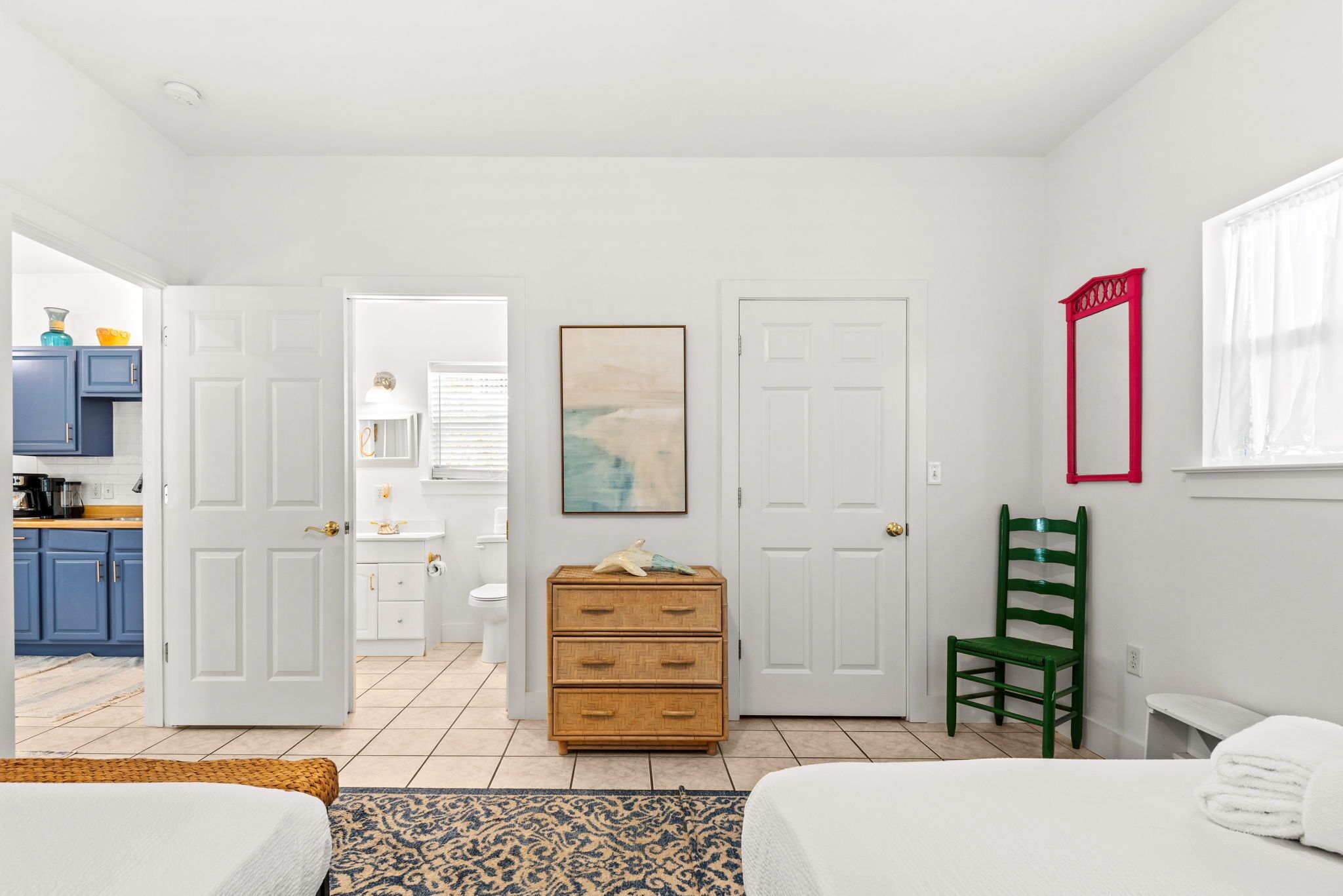 A hotel room with a bed, a dresser, a chair, and a bathroom visible through an open door.