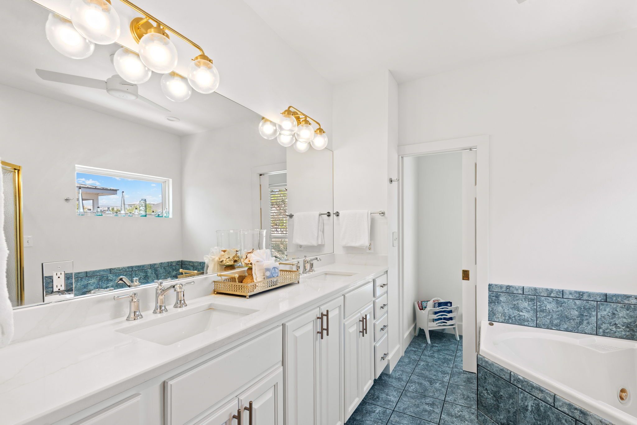 Une salle de bain moderne dotée d’un grand miroir, de deux vasques, d’une baignoire et d’un ventilateur de plafond.