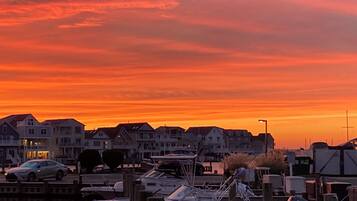 A marina with boats docked, a row of houses in the background, and a sunset sky.