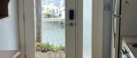 A kitchen with a refrigerator, a clock, and a door leading to a view of a body of water.