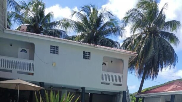 A pool area with a large planter, a building with balconies, and palm trees in the background. - Cozy 1-Bedroom Studio in the Heart of Enchanting Rodney Bay–Fully AirConditioned (Rodney Bay)