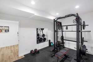 A gym with a squat rack, barbell, weight plates, and a bench. - Lehi Basement: 2 Kings, 4 Queens, Pool & Parks (Lehi)