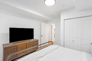 A bedroom with a bed, a TV, a wooden cabinet, and white doors. - Lehi Basement: 2 Kings, 4 Queens, Pool & Parks (Lehi)