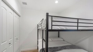 Ein Stockbett mit weißer Matratze und grauer Decke, ein weißer Kleiderschrank mit mehreren Türen und ein Holzboden.