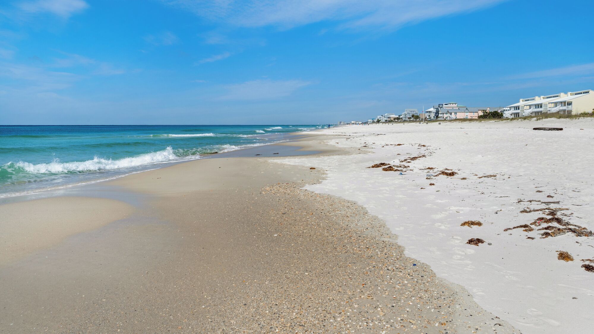 Ein Strand mit weißem Sand, klarem blauen Wasser und einer Reihe weißer Gebäude mit Balkonen.
