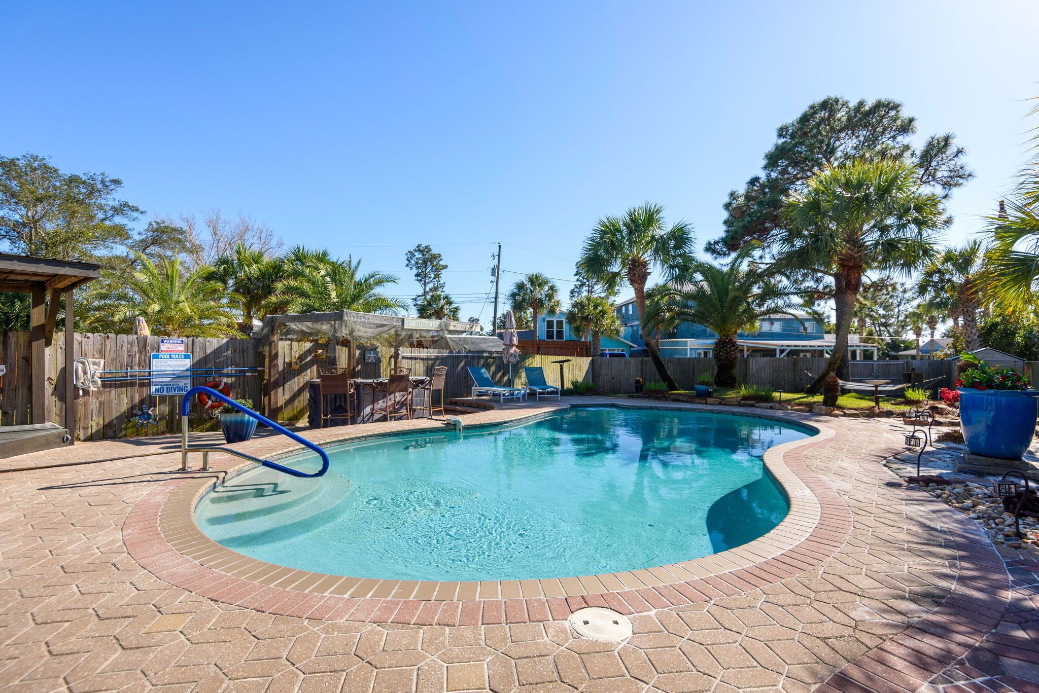 A swimming pool with a wooden deck, palm trees, and a blue sky.