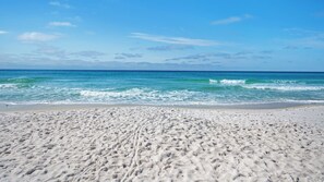 Ein sandiger Strand mit Fußabdrücken, die zum Wasser führen, ein klarer Himmel und sanfte Wellen.