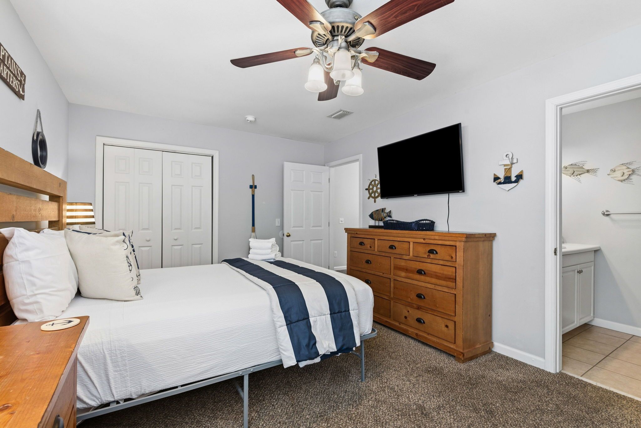 Ein Schlafzimmer mit einem Bett, einem Holzschrank, einem Deckenventilator, einem Fernseher und maritimer Dekoration.