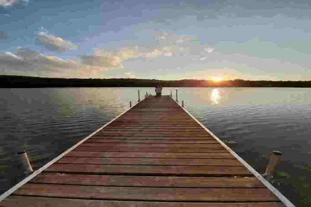 Une jetée en bois s’étendant sur une étendue d’eau calme, avec un coucher de soleil en arrière-plan.