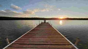 A wooden pier extending into calm water with a sunset in the background.
