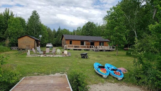 A wooden dock leading to a river, a small cabin, and a larger building with a deck. - Lakefront Wooden Cabin 1.5 hours from Ottawa (Messines)