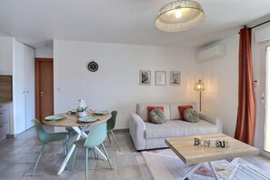 A modern living room with a sofa, coffee table, dining table with chairs, and a hanging light fixture. - Le Dolce Verde | Downtown, beaches & parking (Ajaccio)