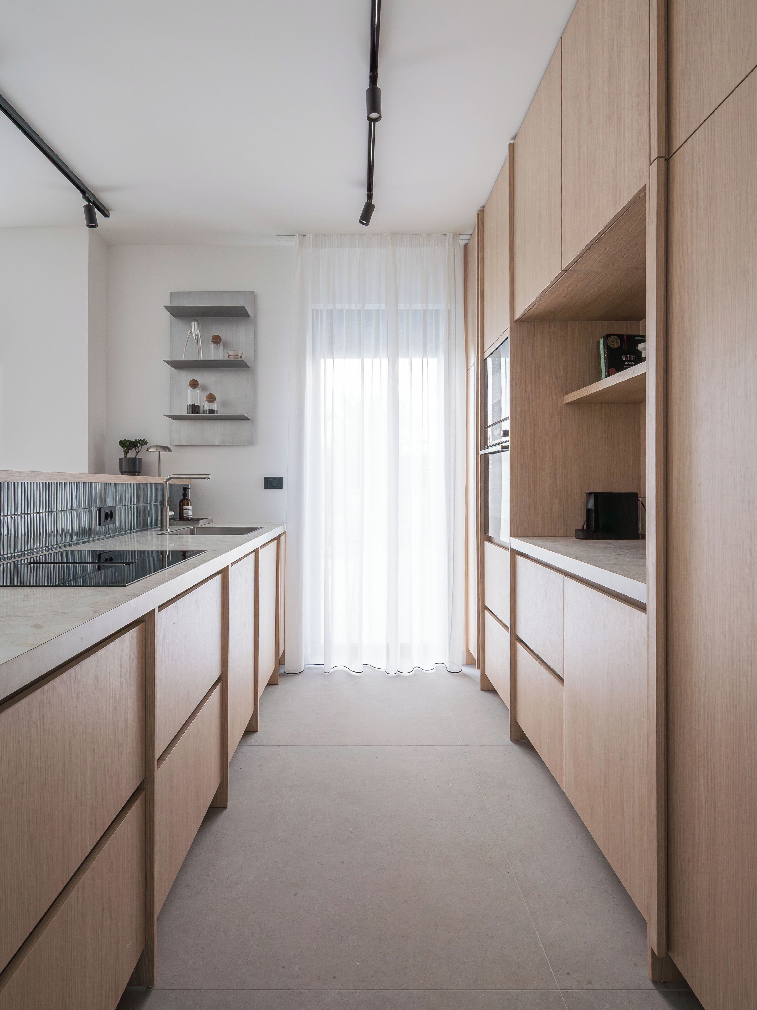 Una cocina moderna con armarios de madera, estufa integrada y una ventana con cortinas translúcidas.