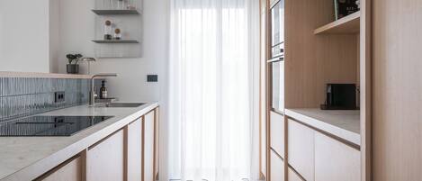 Una cocina moderna con armarios de madera, estufa integrada y una ventana con cortinas translúcidas.