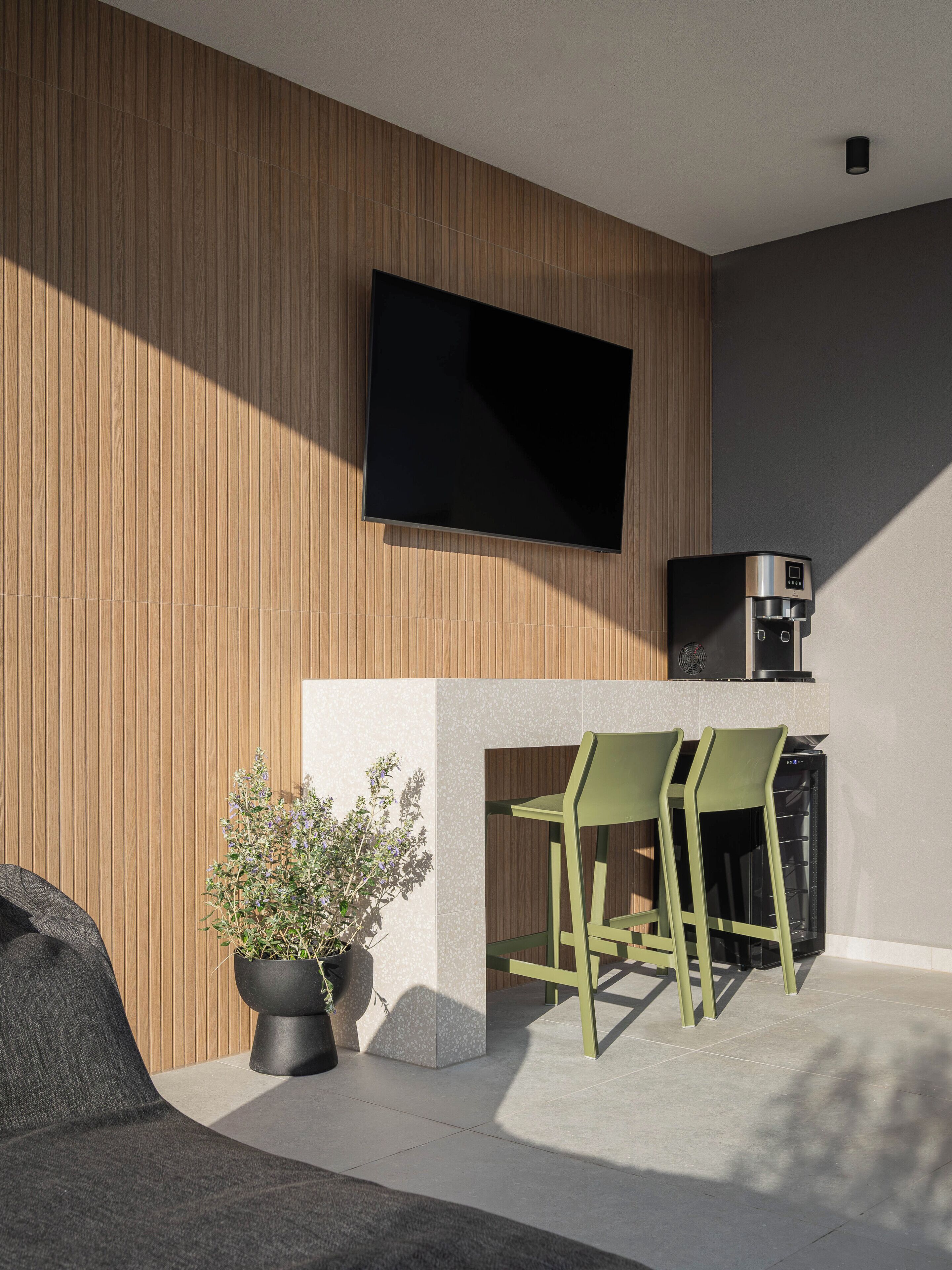 A modern outdoor seating area with a flat-screen TV, a coffee machine, and a potted plant.
