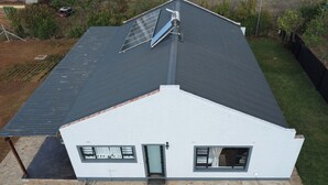 A house with a sloped roof, solar panels, a stone foundation, and a small front porch. - Perfect 2 Bedroom Farmhouse Close to Bulawayo CBD (Bulawayo)
