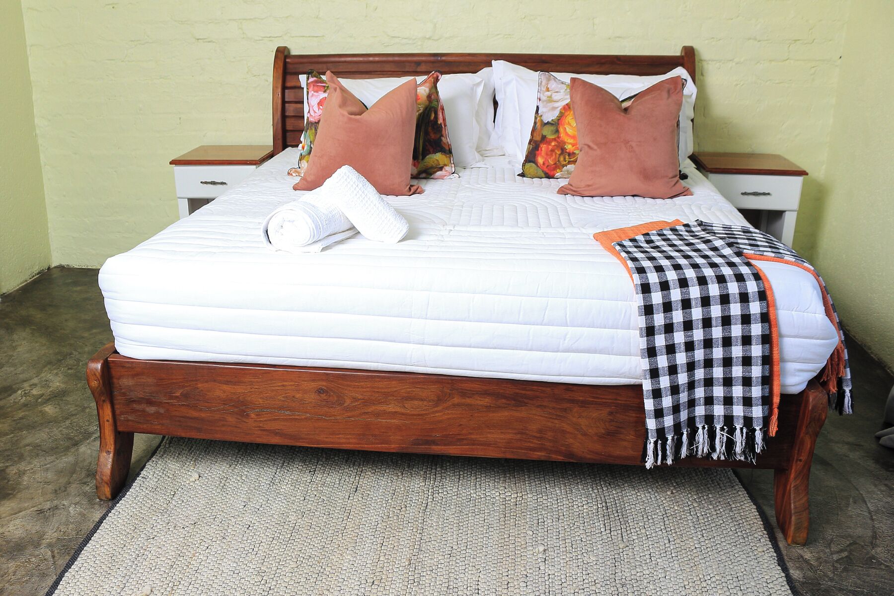 A neatly made bed with a white quilt, two wooden nightstands, and a checkered throw blanket.