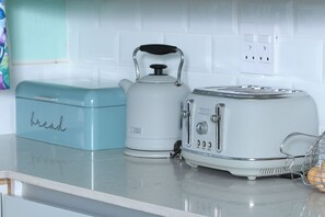 Een keuken met een broodrooster, een waterkoker en een broodbak op een aanrecht.