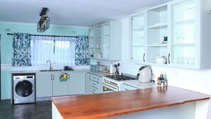 A kitchen with white cabinets, a wooden countertop, a washing machine, and a window with curtains. - Perfect 2 Bedroom Farmhouse Close to Bulawayo CBD (Bulawayo)