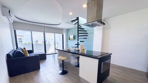 Une cuisine moderne dotée d’un îlot central, d’un coin repas avec une table et des chaises, et d’un canapé agrémenté de coussins.