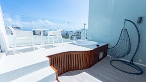 Une terrasse sur le toit avec un jacuzzi, des chaises blanches et un fauteuil suspendu.