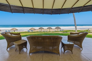 A covered outdoor seating area with wicker furniture and a view of the beach.