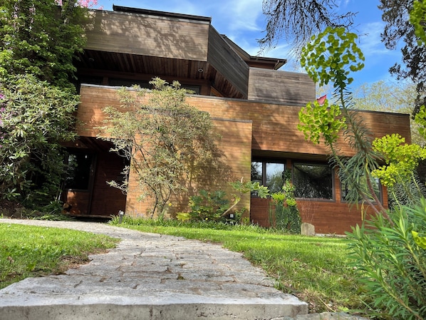 Une maison moderne avec un chemin de pierre menant à l’entrée, entourée de verdure.