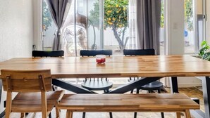 Un comedor con mesa y bancos de madera, una araña y vistas al exterior a través de amplios ventanales.