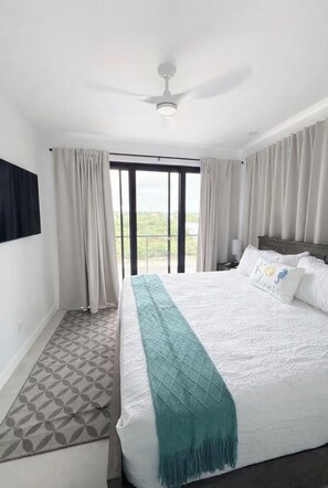A hotel room with a bed, a ceiling fan, a large window with curtains, and a view of the outdoors. - 4-bedroom Estate with Two Separate Villa (Providenciales)