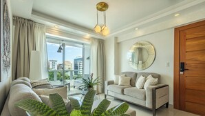 Una sala de estar moderna con un sofá, una mesa de centro, una planta grande, un espejo redondo y vistas de la ciudad a través de amplios ventanales.
