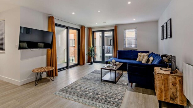 Een moderne woonkamer met een flatscreen televisie, een blauwe bank, een salontafel en een houten kast.