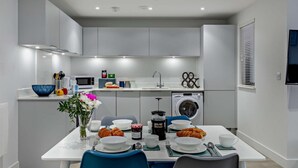 Een moderne keuken met een eethoek, witte kasten, een magnetron, een spoelbak en een wasmachine.