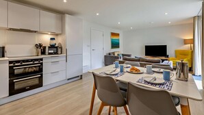A modern kitchen with built-in appliances, a dining area with a table set for two, and a living area with a sofa and TV. - Mist - Luxury Cottages (Woolacombe)