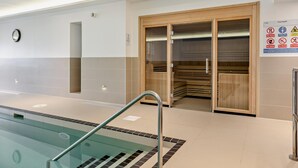 A modern indoor pool area with clear signage, a clock, and a sauna. - Mist - Luxury Cottages (Woolacombe)