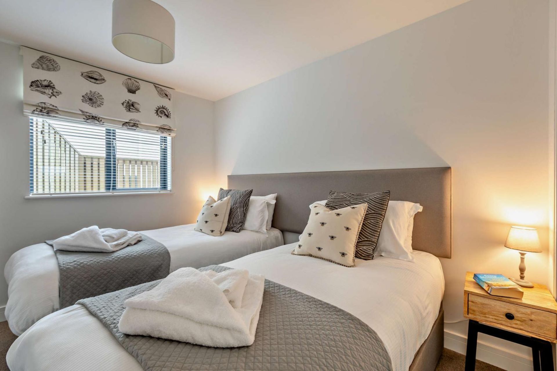 Een slaapkamer met twee bedden, een raam met zonwering, een nachtkastje met lamp en een wand met patroon.