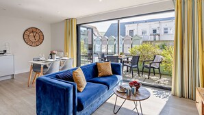 Una sala de estar moderna con un sofá azul, un comedor con mesa y sillas, y un ventanal con cortinas.