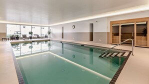 Una piscina interior con vista despejada al área de la piscina, un reloj en la pared y una zona de estar con sillas y mesas.