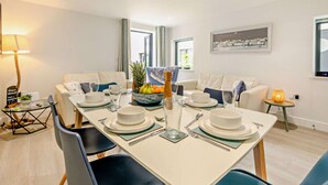 A dining area with a table set for four, chairs, a bowl of fruit, and a lamp. - Waveside - Luxury Cottages (Woolacombe)