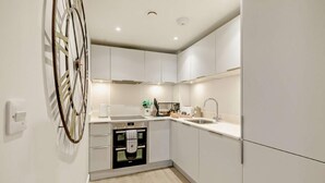 A modern kitchen with white cabinetry, a built-in oven, a sink, and a coffee maker. - Waveside - Luxury Cottages (Woolacombe)
