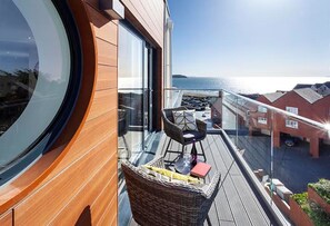 A balcony with a wicker chair, a small table, and a balcony railings. - Reefside - Luxury Cottages (Woolacombe)