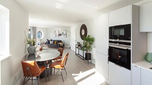 A modern kitchen with built-in appliances, a dining area with a round table and chairs, and a living area with a sofa and decorative items. - Reefside - Luxury Cottages (Woolacombe)