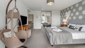 Ett modernt hotellrum med en säng, en hängstol, en tv och utsikt över badrummet.