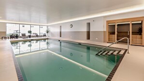 En swimmingpool med en glasvägg som avgränsning, en klocka på väggen och en trädörr med en skjutbar glaspanel.