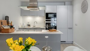 Ett modernt kök med vita skåp, en rostfri köksfläkt, en inbyggd ugn och en klocka på väggen.
