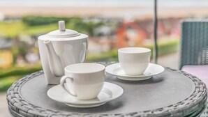 A table with a white teapot and two cups on a woven coaster, overlooking a scenic view. - Wavemist -Luxury Cottages (Woolacombe)